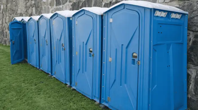 Row of blue portable toilets lined up on grass against a stone wall for event sanitation in Manchester, NH