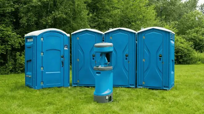 Four blue portable toilets and a matching hand washing station on grass near trees, a common sight at local outdoor events in Manchester, NH