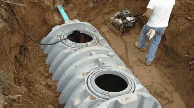 Septic tank installation showing a technician compacting soil around a new poly septic tank in an excavation pit in Manchester, NH